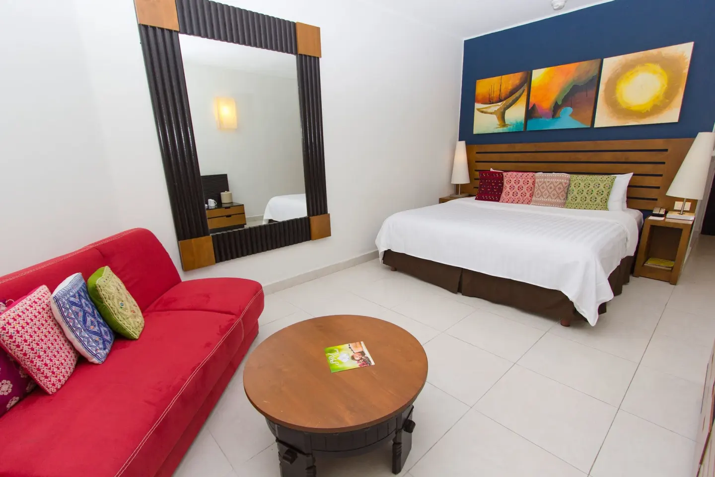 Standard Room with king bed, red sofa, mirror, and coffee table at Grand Decameron Los Cabos.