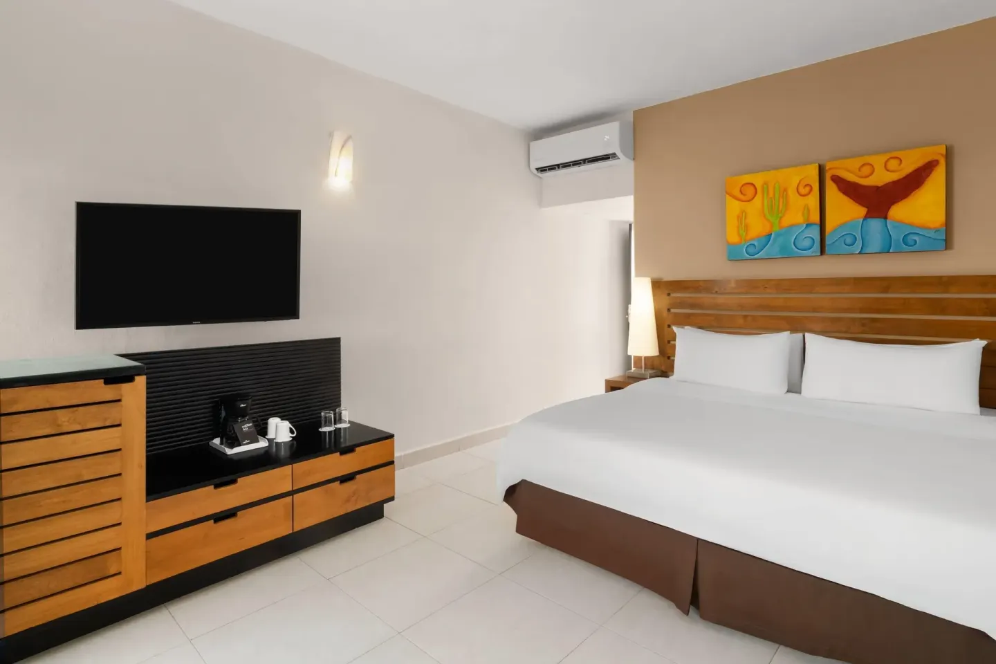 Standard Room with king bed, wall-mounted TV, console, and coffee setup at Grand Decameron Los Cabos.