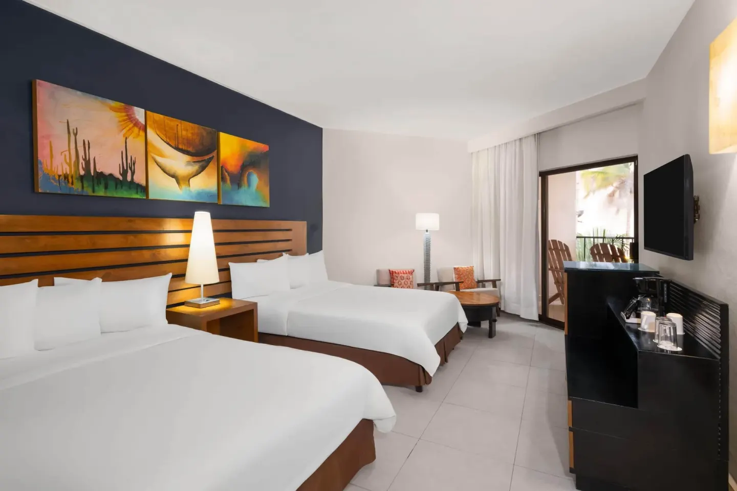 Standard Room with two beds, balcony door, TV, and seating area at Grand Decameron Los Cabos.