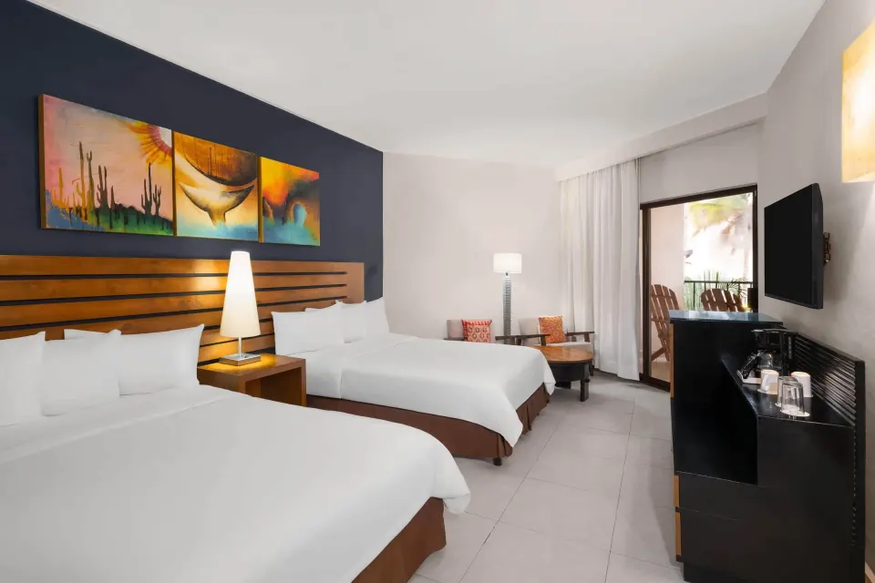 Standard Room with two beds, balcony door, TV, and seating area at Grand Decameron Los Cabos.