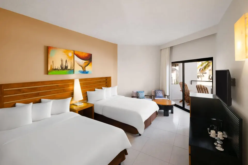 Standard Room with two beds, balcony seating, TV, and coffee setup at Grand Decameron Los Cabos.
