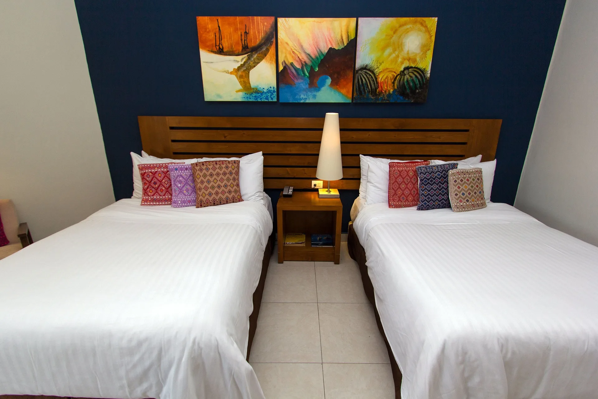 Standard Room with two beds, shared nightstand, lamp, and wall art at Grand Decameron Los Cabos.