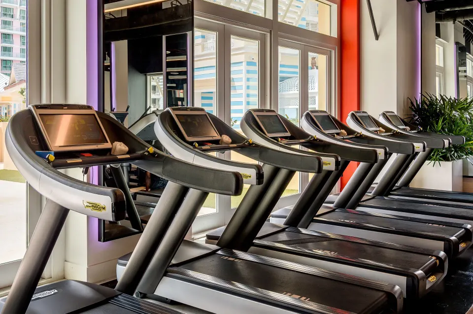 A row of treadmills faces tall windows in the fitness center at Grand Hyatt Baha Mar.