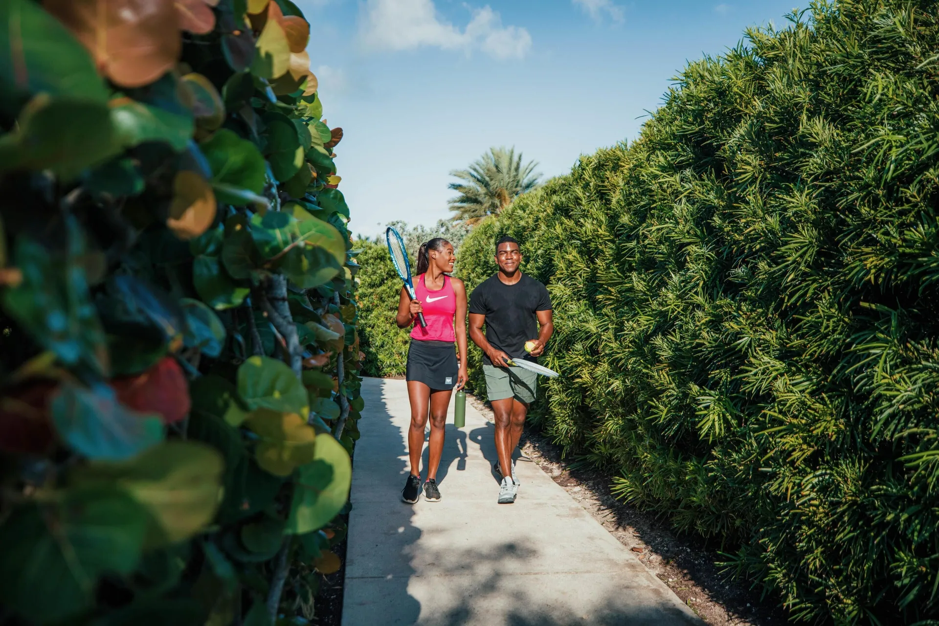 Two guests carrying tennis racquets walk along a garden path at Grand Hyatt Baha Mar.