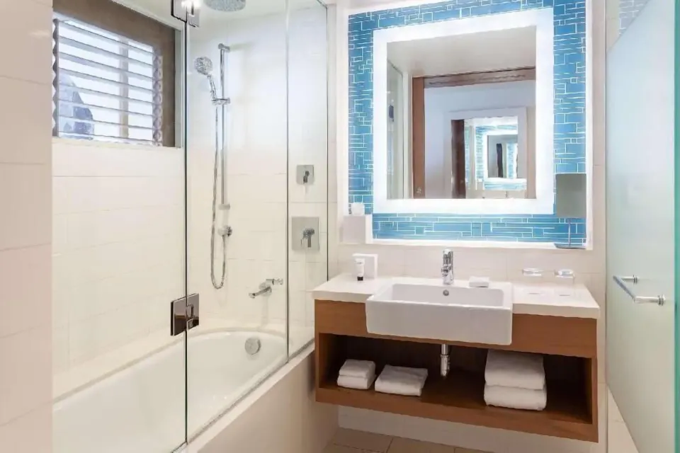 Guest bathroom at Grand Hyatt Baha Mar with glass tub shower, vanity, and blue mirror tile.