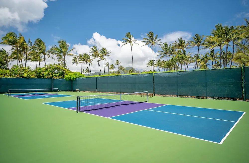 Outdoor pickleball courts at Grand Hyatt Kauai Resort and Spa and Spa bordered by palms and green windscreens.