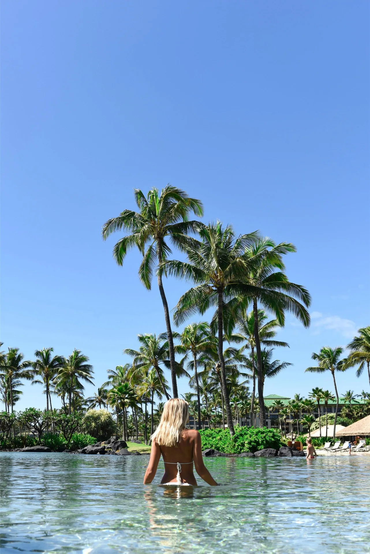 Guest wading in the palm-lined pool at Grand Hyatt Kauai Resort and Spa and Spa.
