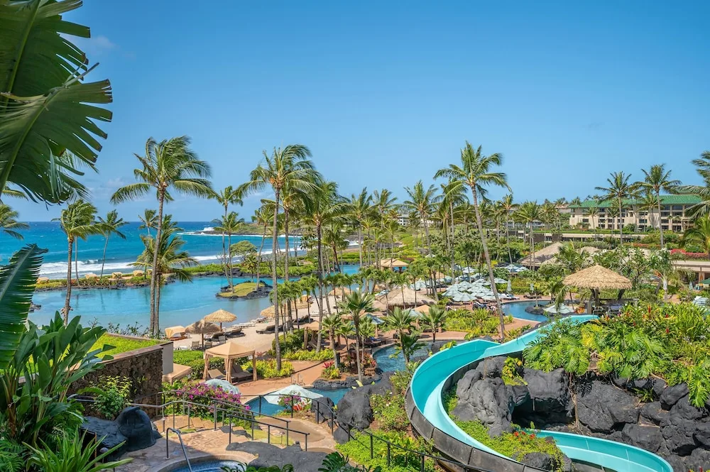 Pool complex with waterslide, palms, and ocean beyond at Grand Hyatt Kauai Resort and Spa and Spa.