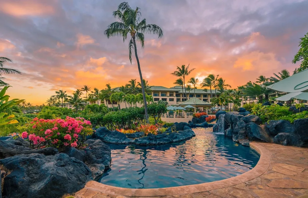 Rock-edged pool and waterfall at sunset at Grand Hyatt Kauai Resort and Spa and Spa.