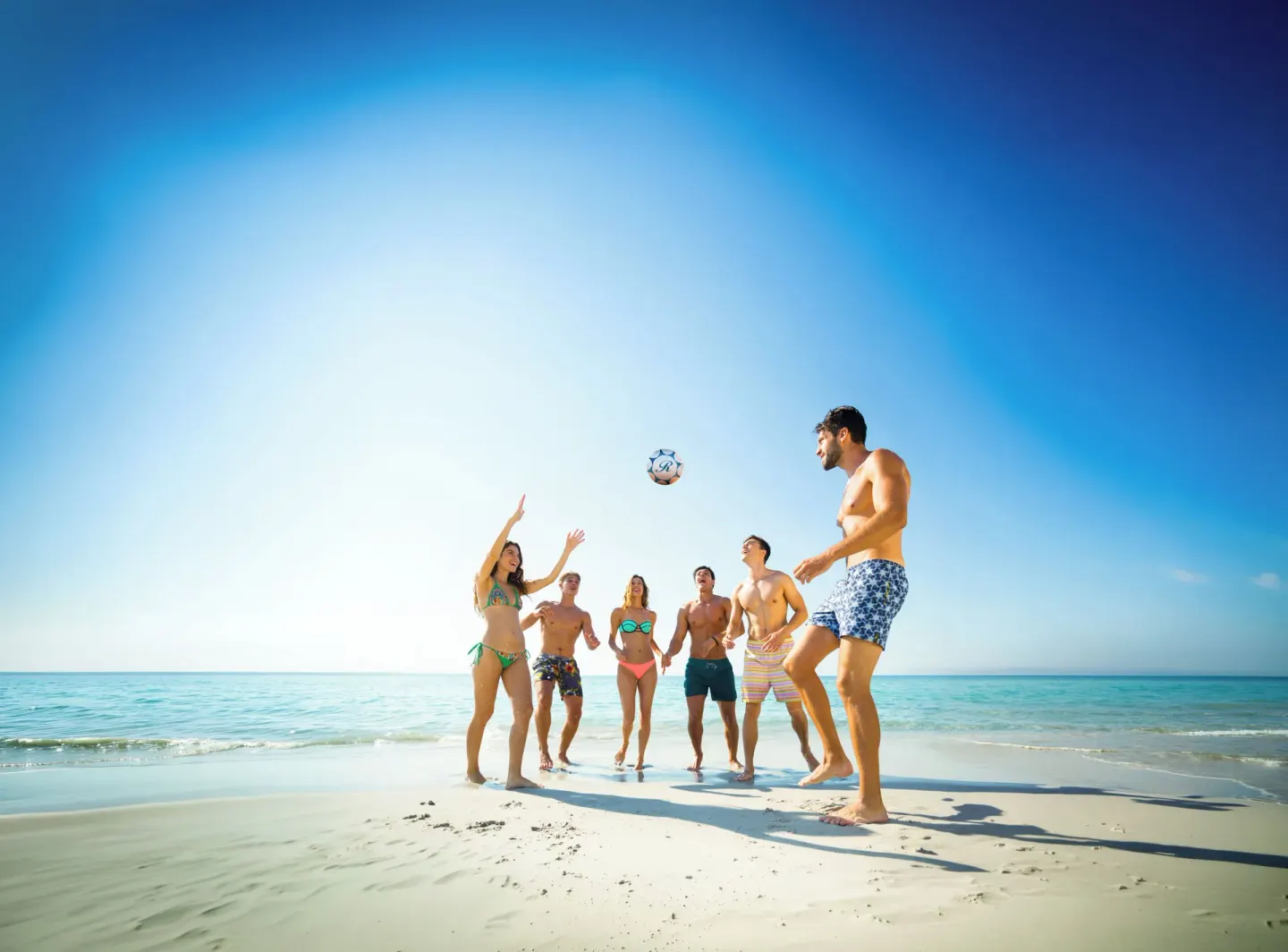 Guests playing beach volleyball at Grand Lido Negril Au-Naturel on bright white sand by the sea.