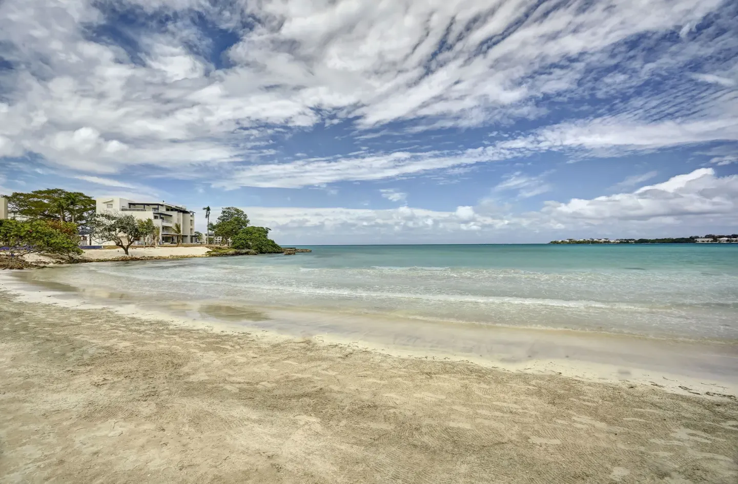 Sandy beach and calm turquoise water at Grand Lido Negril Au-Naturel under a cloud-filled sky.
