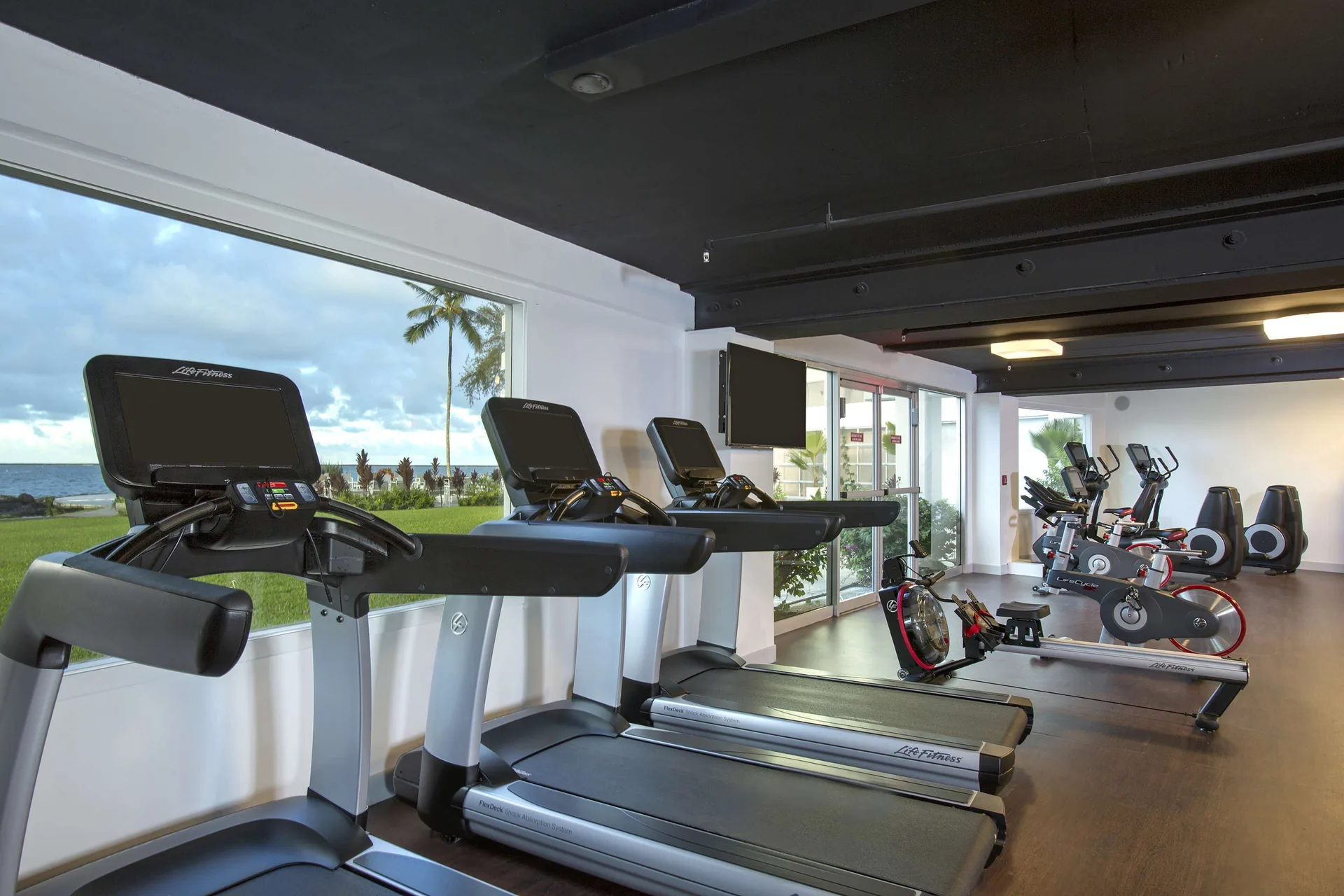 Fitness room treadmills and bikes with ocean-facing windows at Grand Naniloa Hotel Hilo.