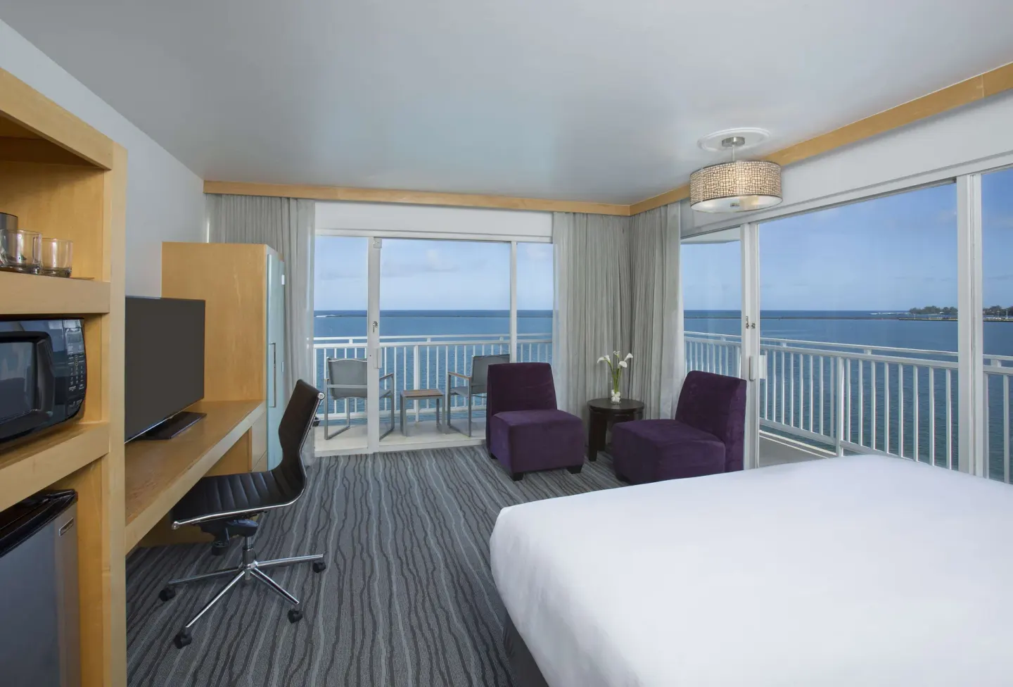 King guest room at Grand Naniloa Hotel Hilo with corner windows, balcony seating, and ocean views.