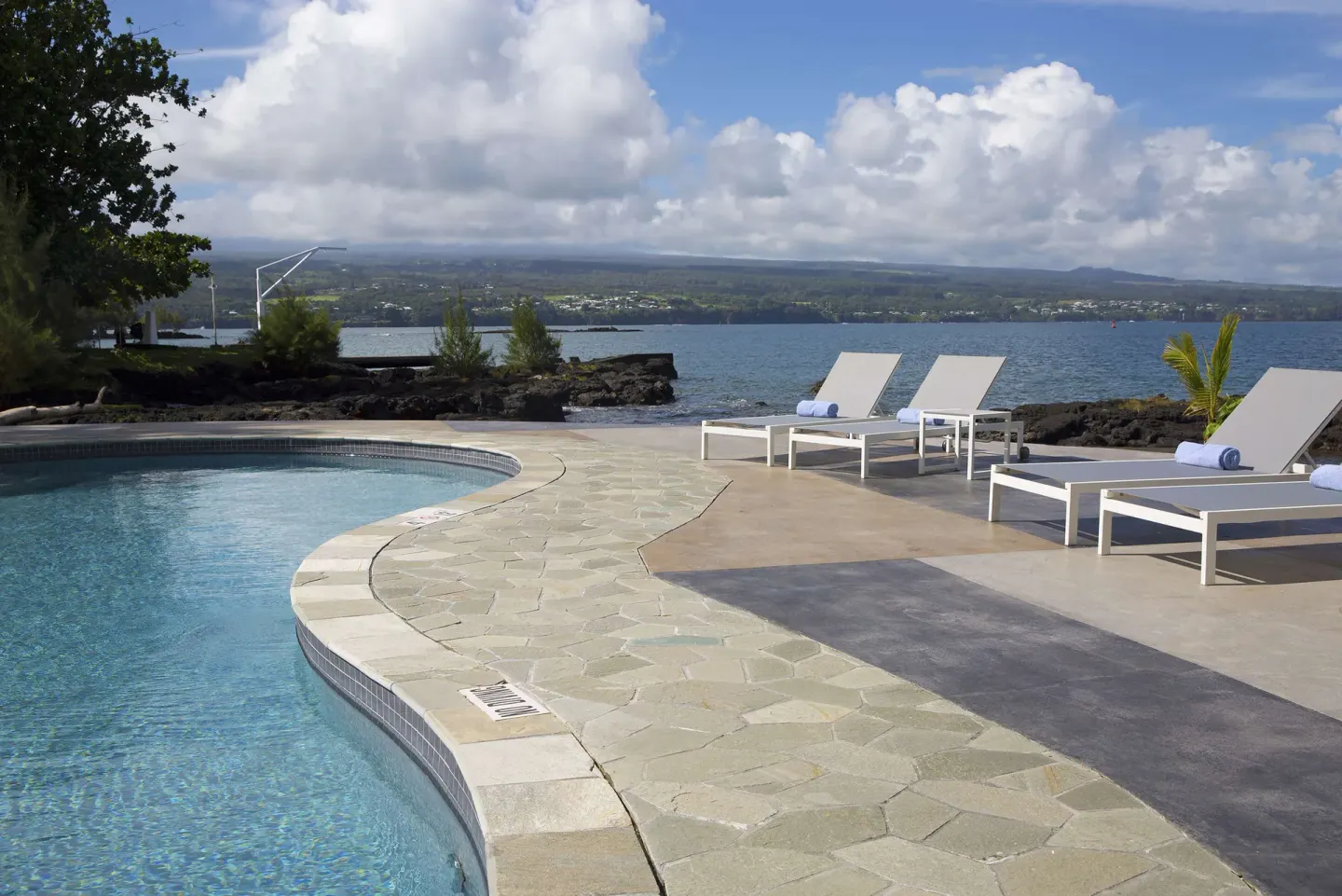 Curved pool, lounge chairs, and oceanfront patio at Grand Naniloa Hotel Hilo.