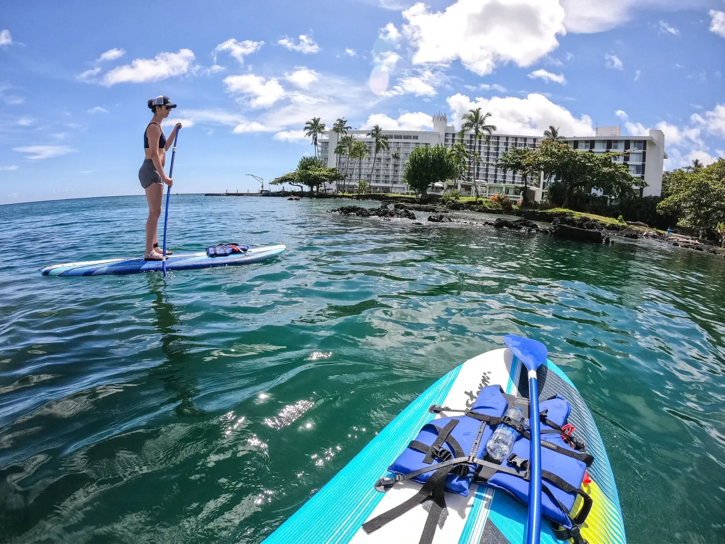 Paddleboards float on Hilo Bay with Grand Naniloa Hotel Hilo in the background.