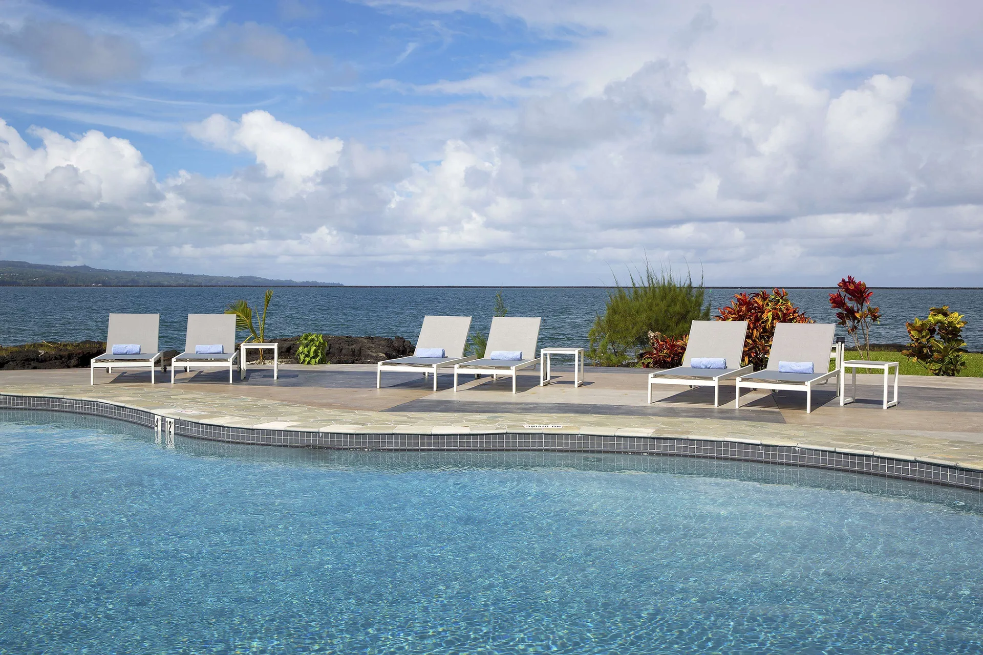 Pool edge with white lounge chairs facing the ocean at Grand Naniloa Hotel Hilo.