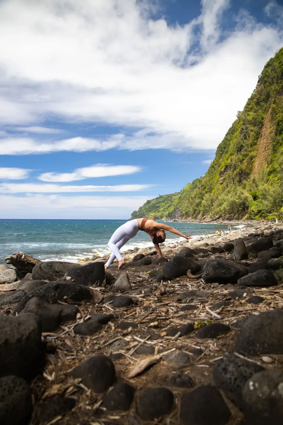 A person does a backbend on a rocky coast near Grand Naniloa Hotel Hilo.