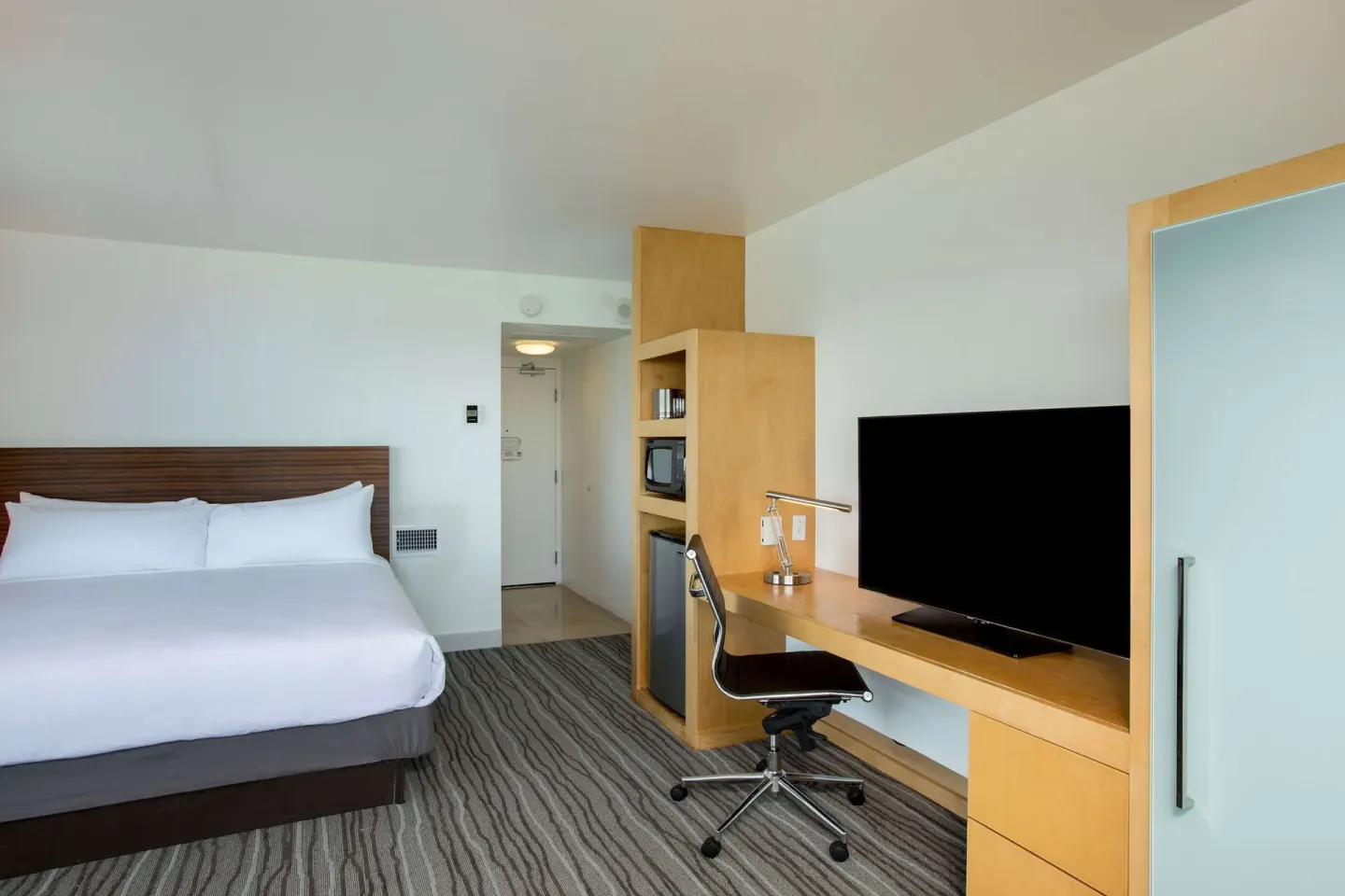 King guest room at Grand Naniloa Hotel Hilo with a bed, desk, television, shelving, and wardrobe.