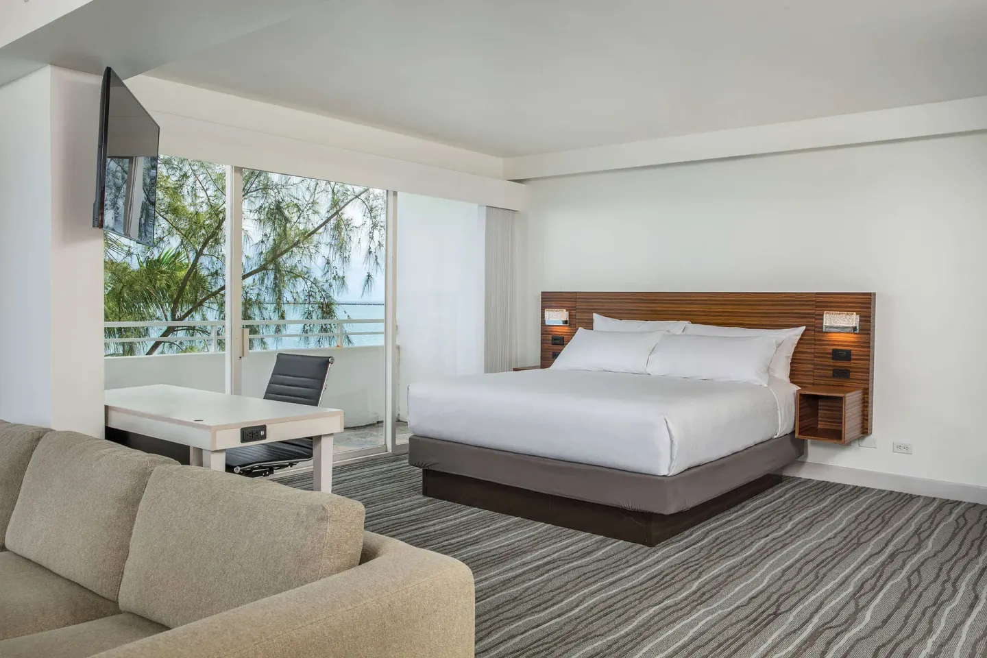 Junior suite king bed, sofa, desk, and balcony windows at Grand Naniloa Hotel Hilo.
