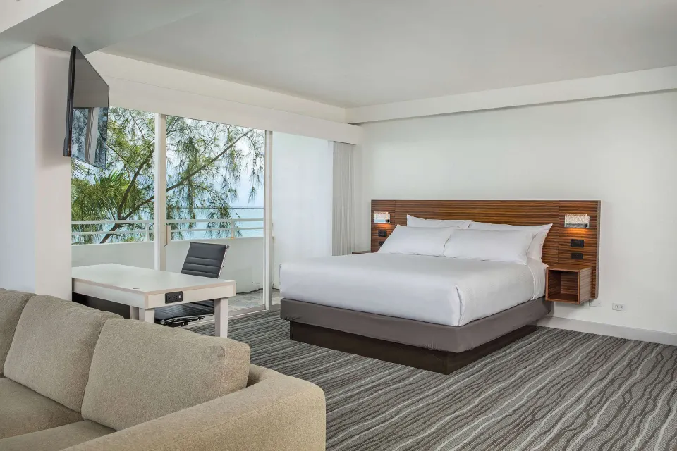 Junior suite king bed, sofa, desk, and balcony windows at Grand Naniloa Hotel Hilo.