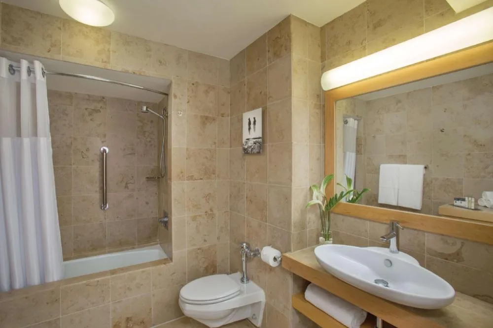 Tiled guest bathroom with sink, mirror, and shower at Grand Naniloa Hotel Hilo.