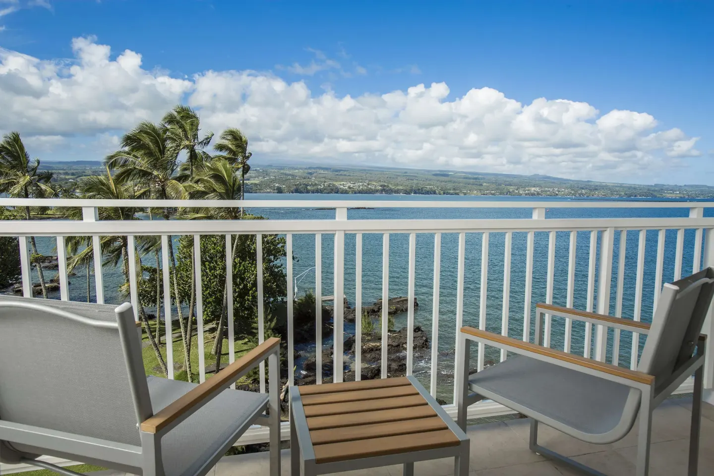 Furnished oceanfront lanai with bay and palm tree views at Grand Naniloa Hotel Hilo.