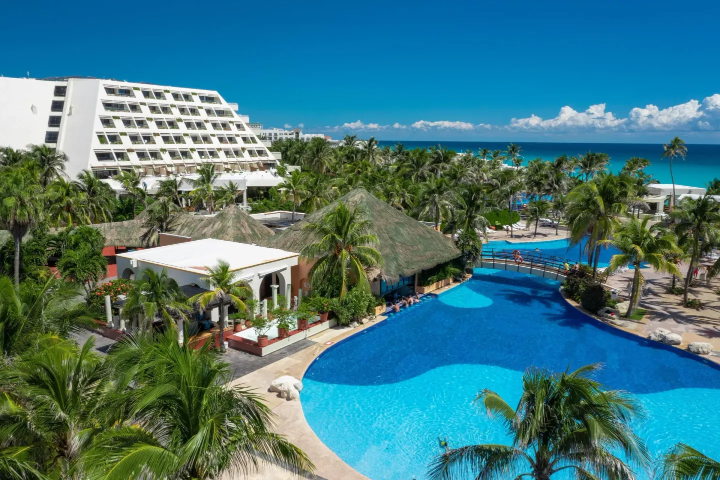 Aerial view of pools, palms, resort buildings, and ocean at Grand Oasis Cancun.