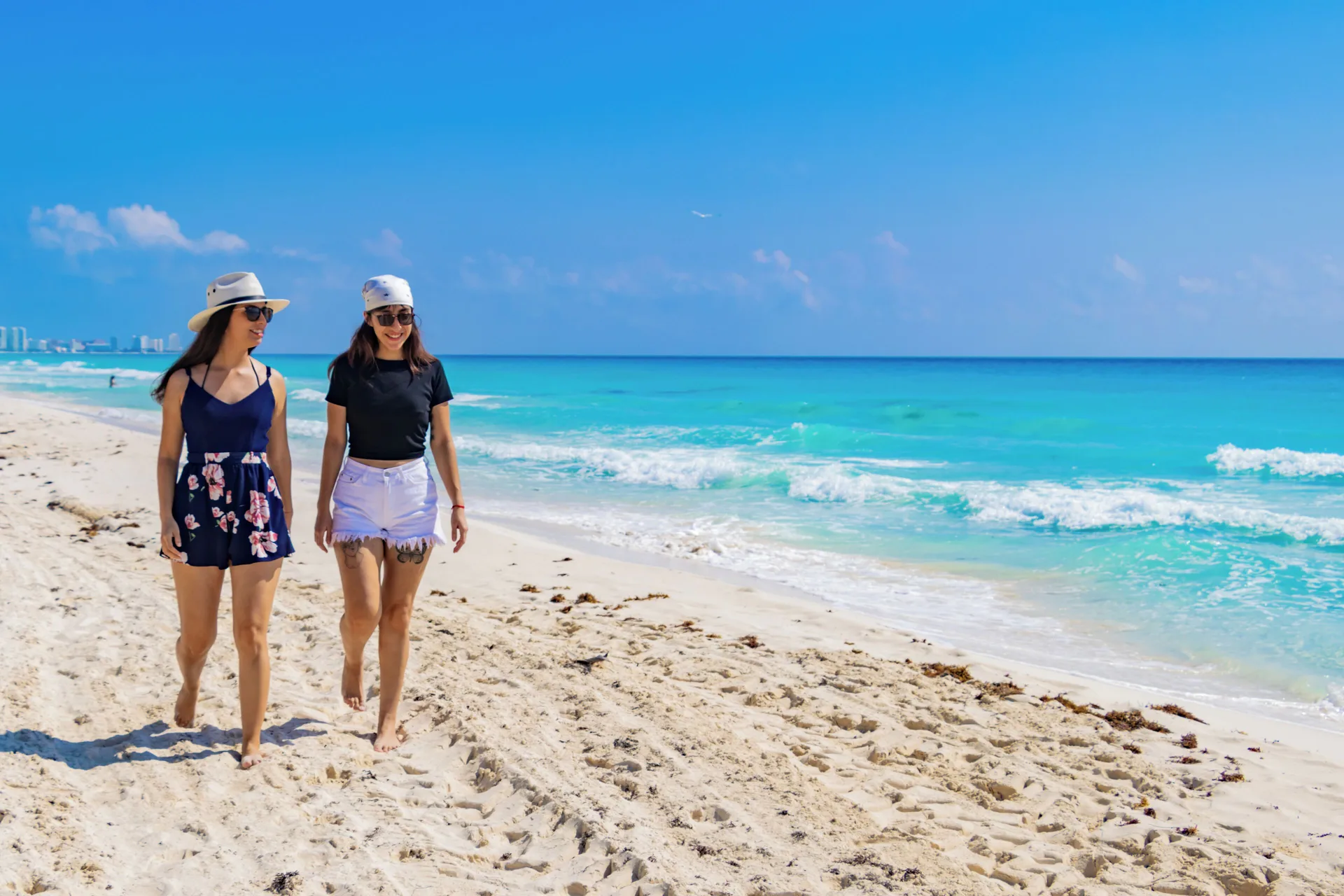 Two women walk beside turquoise water on the beach at Grand Oasis Cancun.