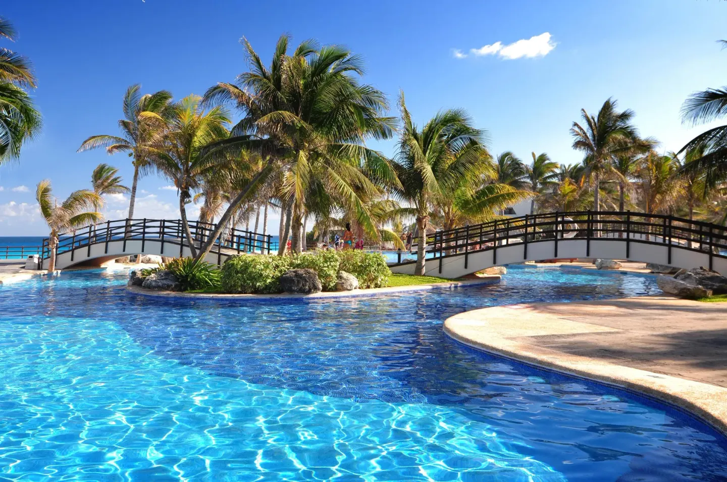 Palm-lined pool with footbridges and ocean beyond at Grand Oasis Cancun.