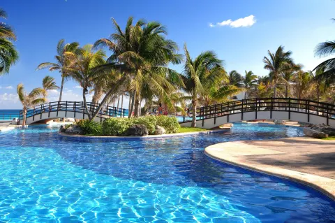 Palm-lined pool with footbridges and ocean beyond at Grand Oasis Cancun.