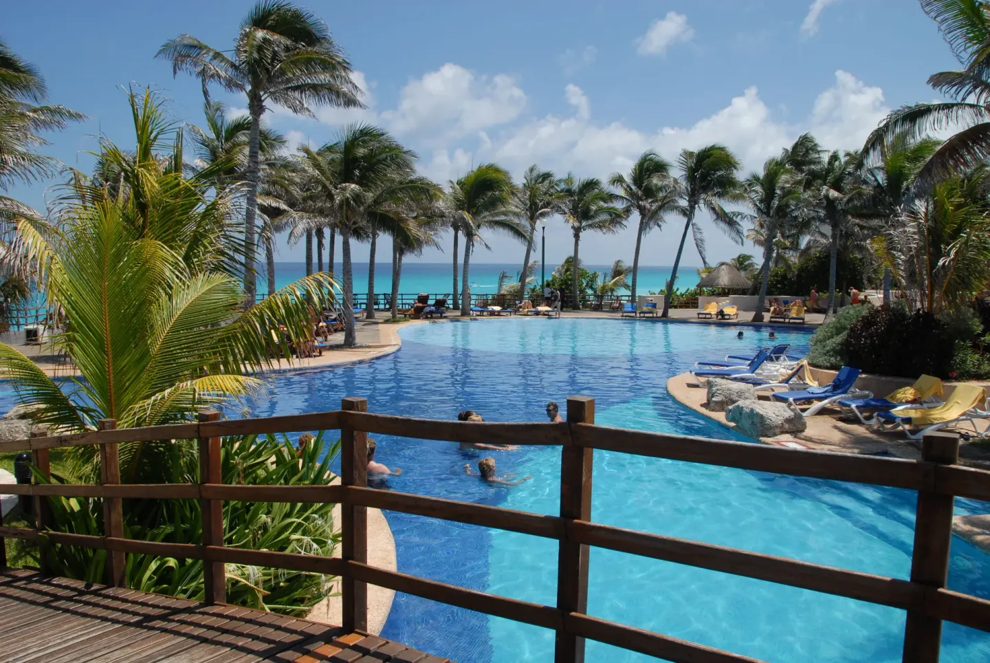 Pool with swimmers, lounge chairs and oceanfront palms at Grand Oasis Cancun.