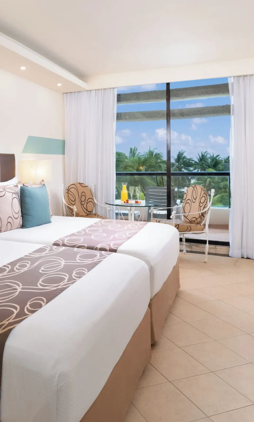 Grand Standard double beds at Grand Oasis Cancun with chairs by a palm-view window.