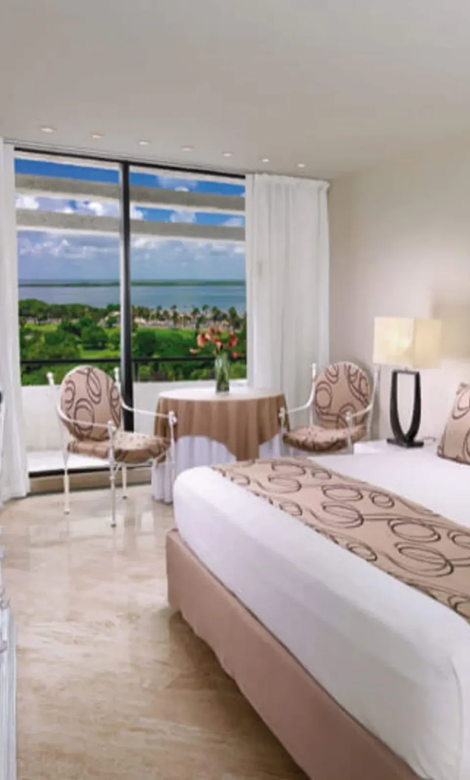 Grand Standard king bed at Grand Oasis Cancun with chairs by a large window and water view.