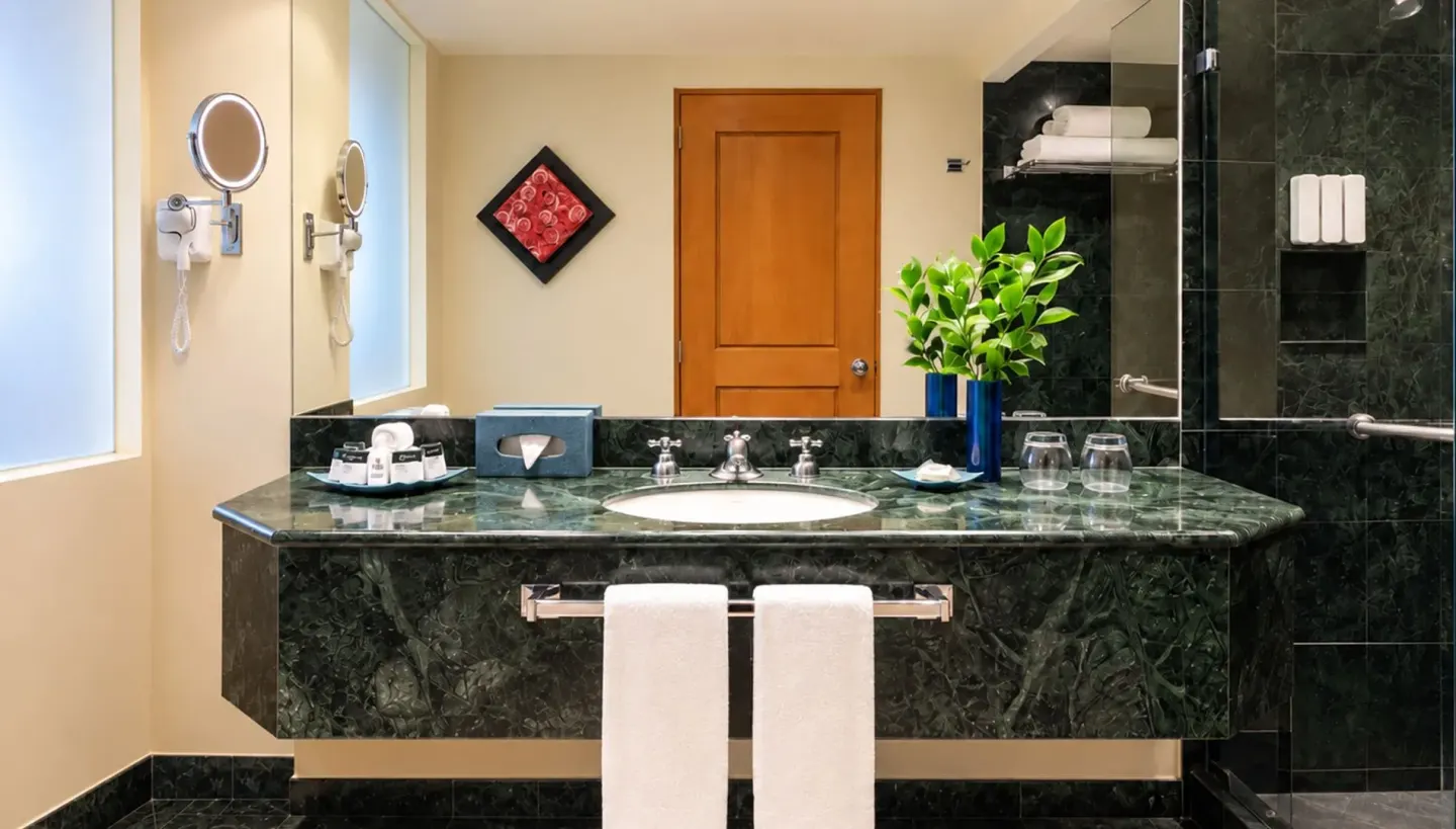 Grand Sunset View bathroom at Grand Oasis Cancun with green marble vanity, mirror, towels, and glass shower.