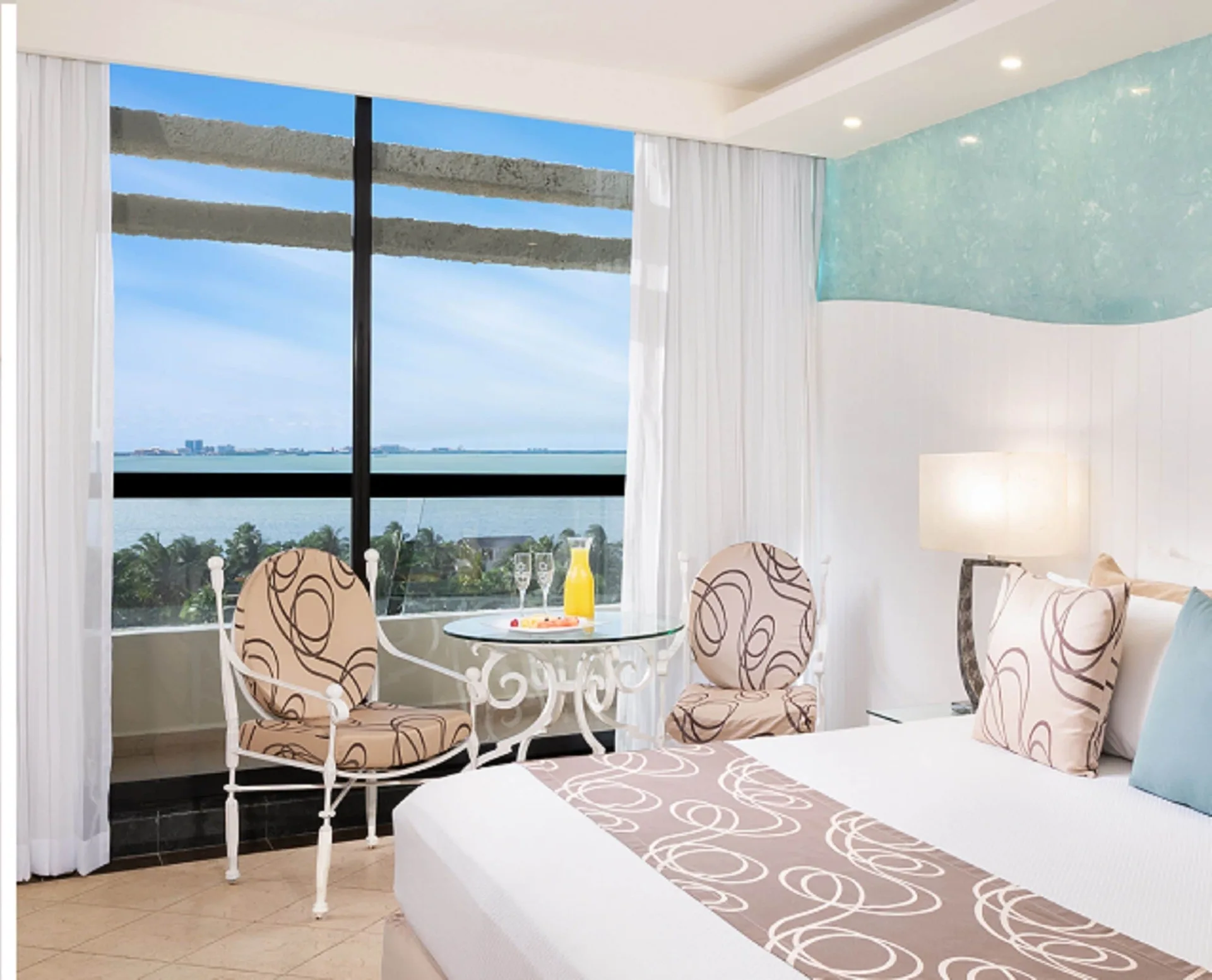 Grand Sunset View king bed room with chairs, glass table, and water view at Grand Oasis Cancun.