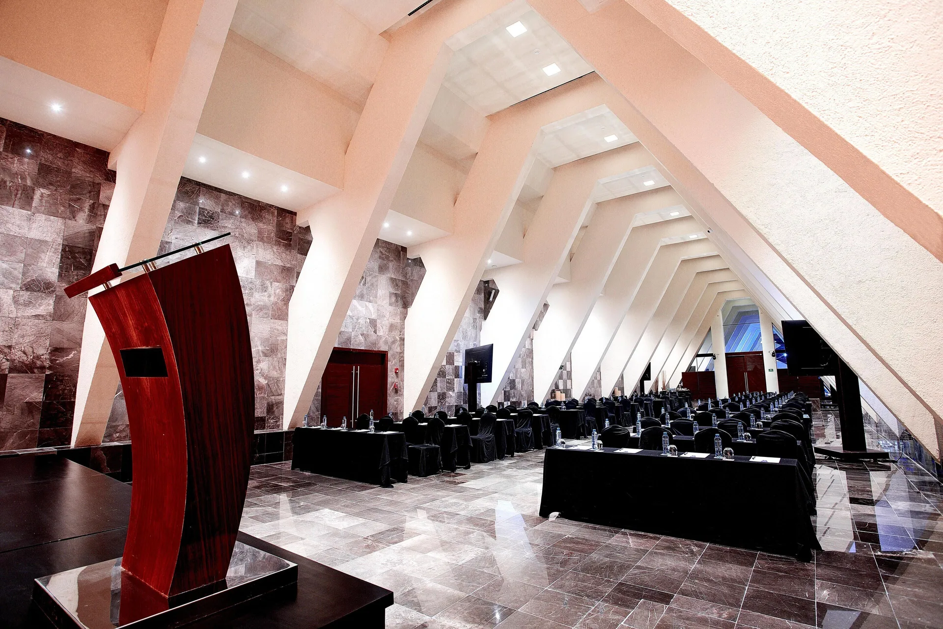 Event room with angular ceiling beams, podium, and black-draped tables at Grand Oasis Cancun.