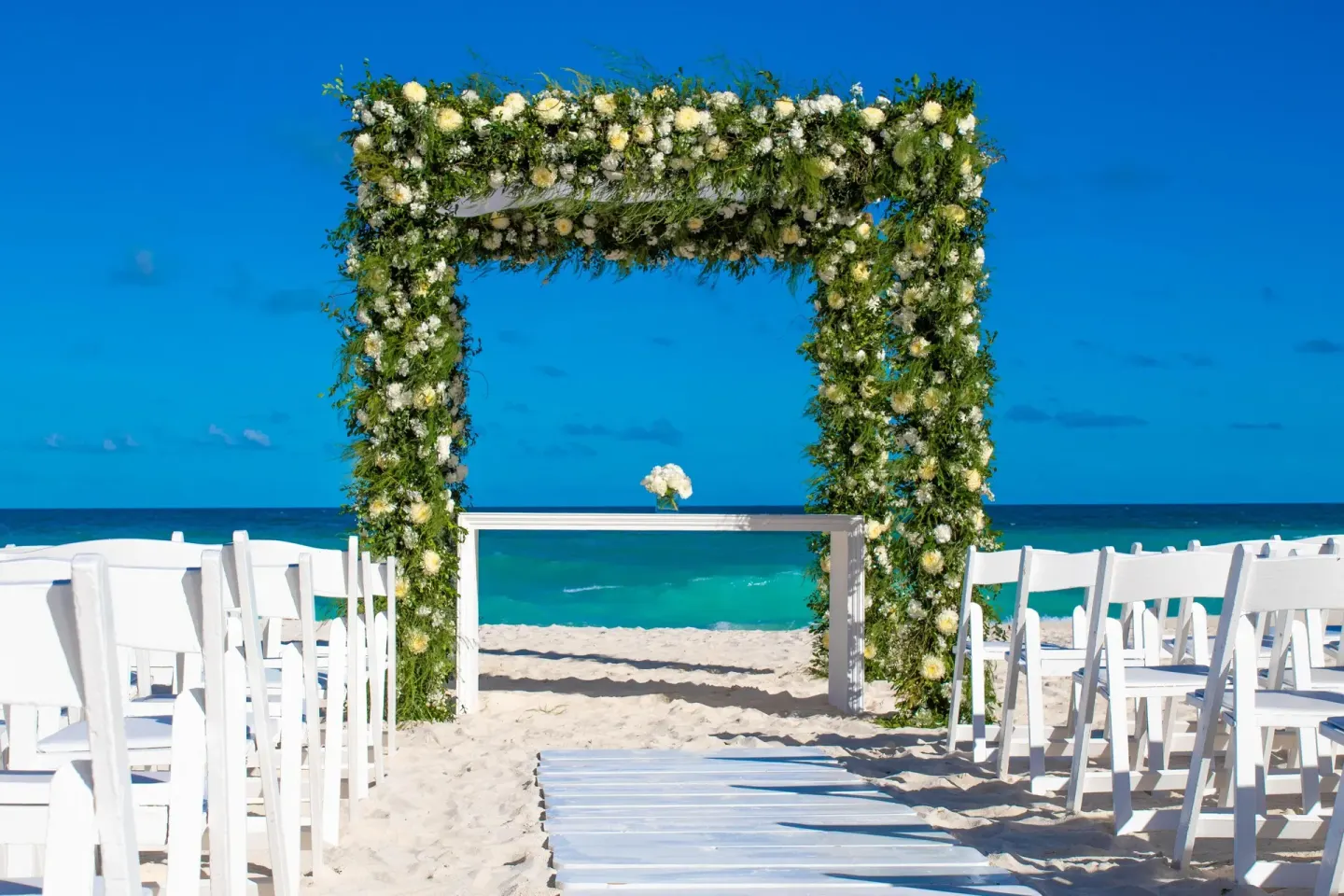 Beach wedding ceremony setup with floral arch and white chairs at Grand Oasis Cancun.