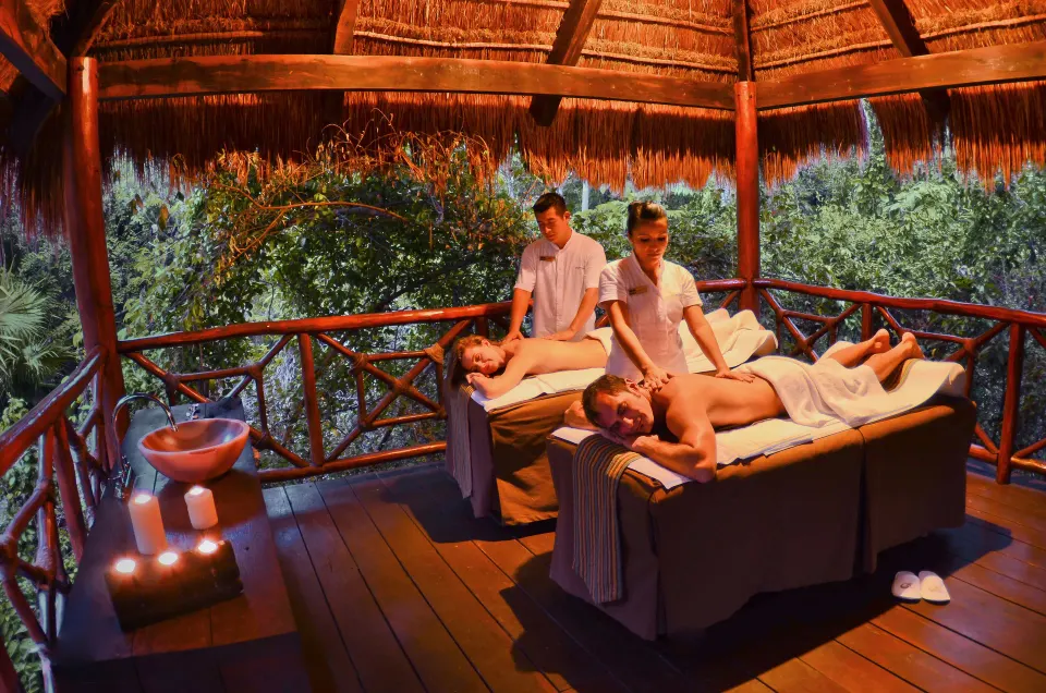 Couples receiving massages in a thatched outdoor spa pavilion at Grand Palladium Colonial Resort & Spa