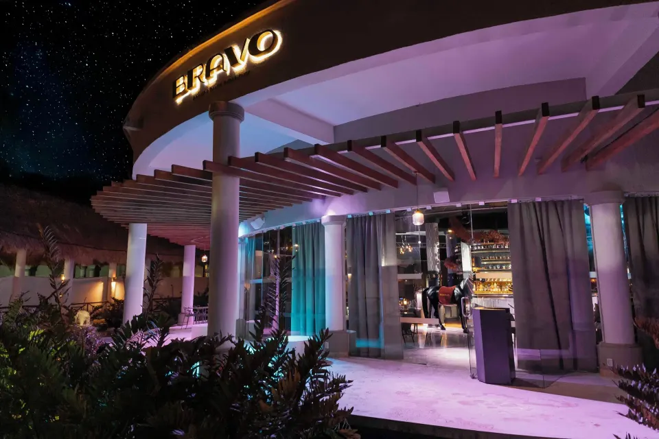 Outdoor entrance to a nighttime bar with illuminated signage at Grand Palladium Colonial Resort & Spa