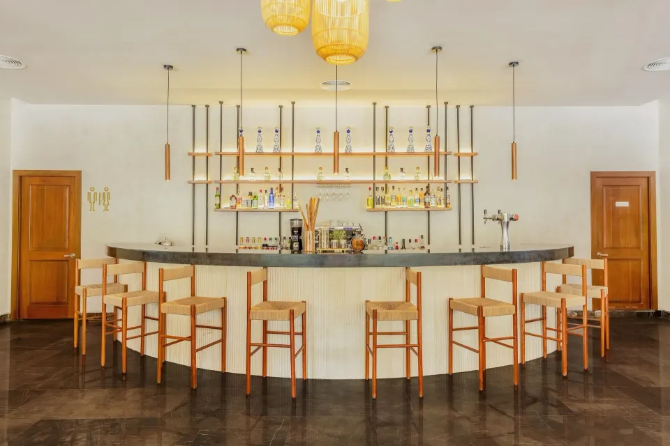 Curved white marble bar with wooden stools and back shelving at Grand Palladium Colonial Resort & Spa