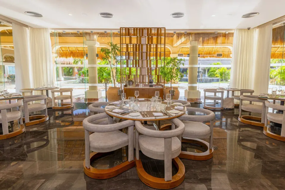 Round table arrangement in a bright restaurant room with floor-to-ceiling windows at Grand Palladium Colonial Resort & Spa