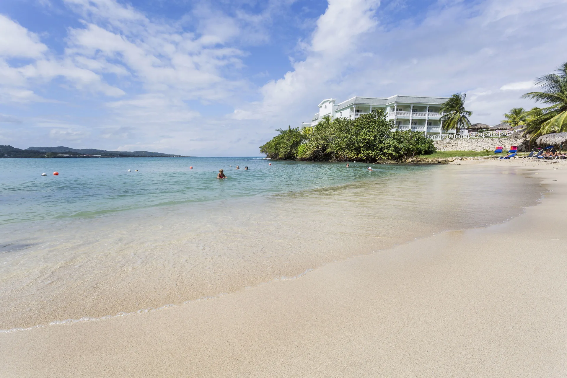Calm sandy beach with swimmers and resort buildings at Grand Palladium Jamaica Resort & Spa.