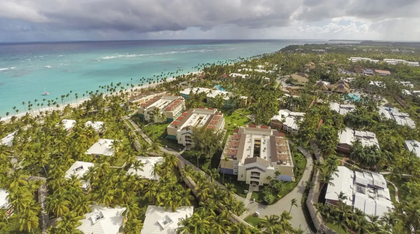 Aerial view of resort buildings, palms, beach, and cloudy sky at Grand Palladium Palace Resort Spa & Casino.
