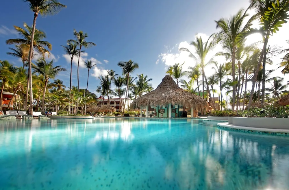 Palm-lined pool with a thatched swim-up bar at Grand Palladium Palace Resort Spa & Casino.