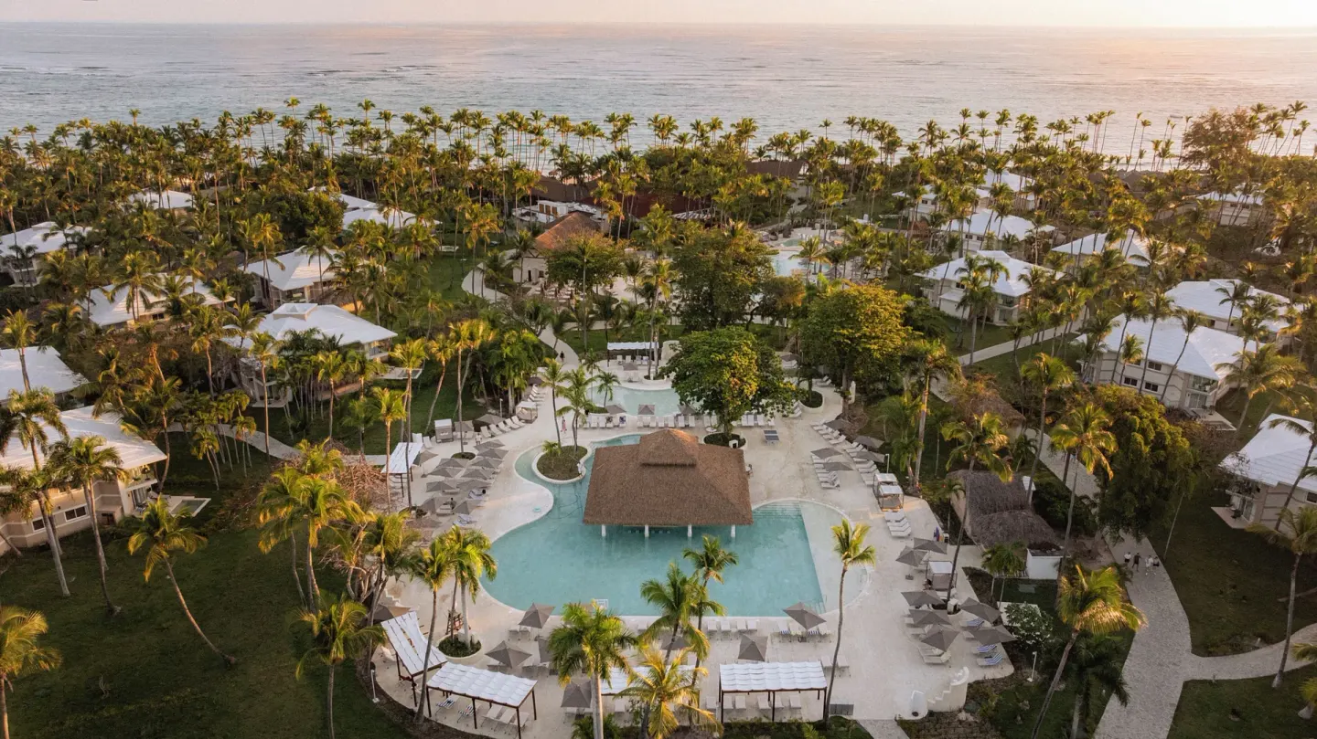 Aerial view of the pool, palms, and beachfront at Grand Palladium Select Bávaro.