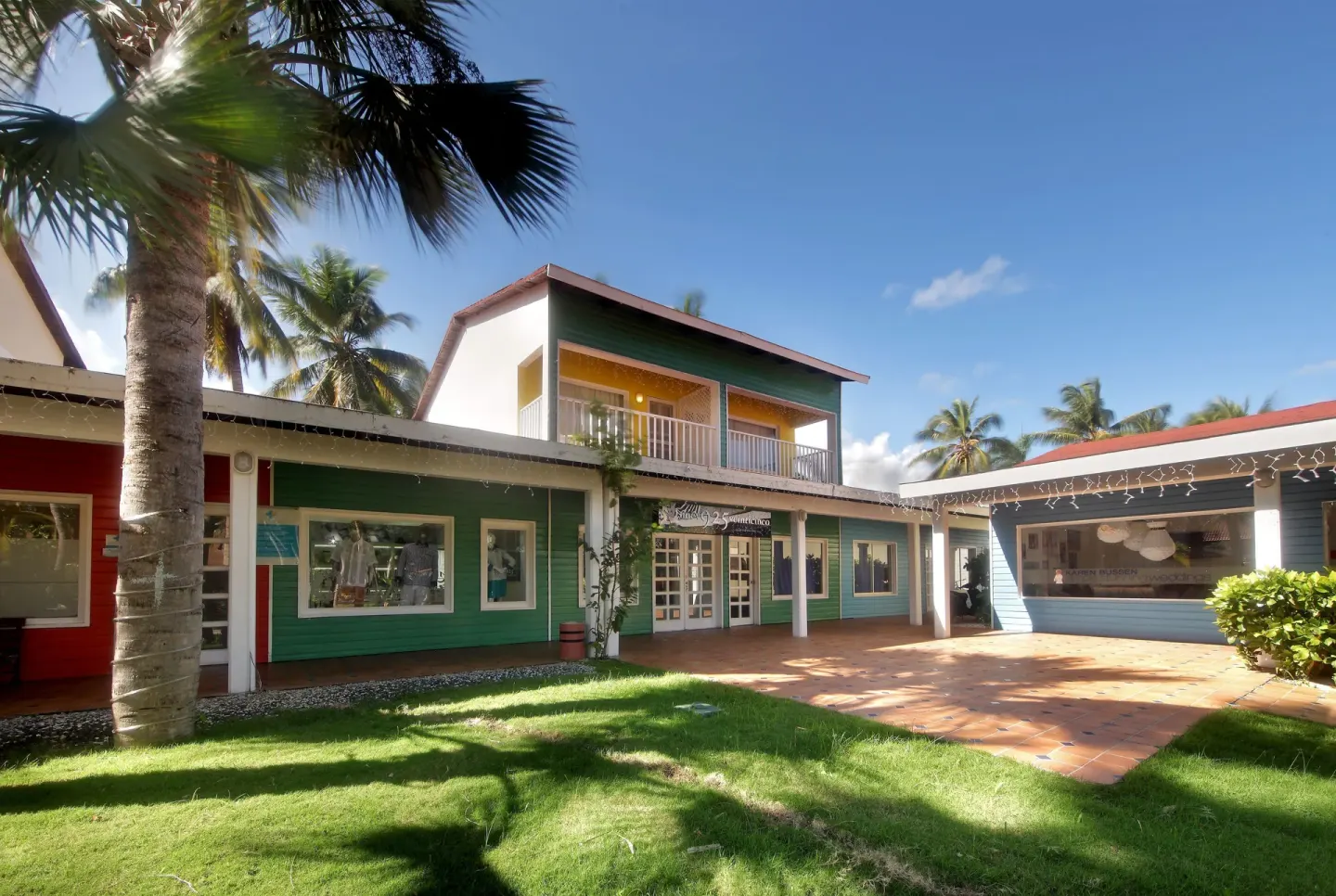 Colorful resort building with shops and palm trees at Grand Palladium Select Bávaro.