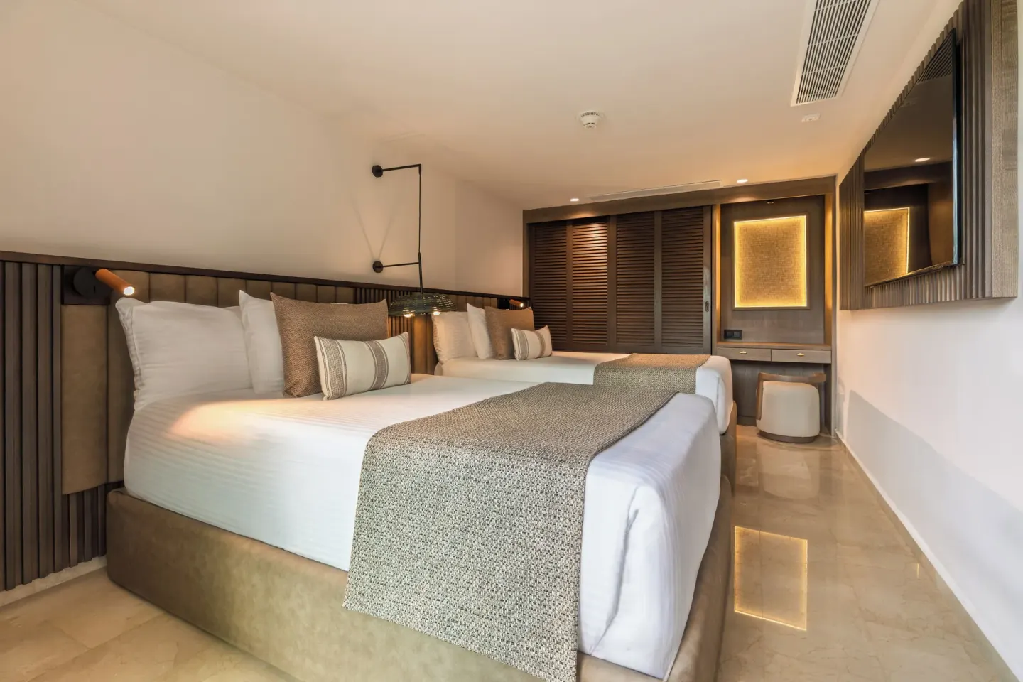 Two-bed guest room with vanity and wall-mounted TV at Grand Palladium Select Bávaro.