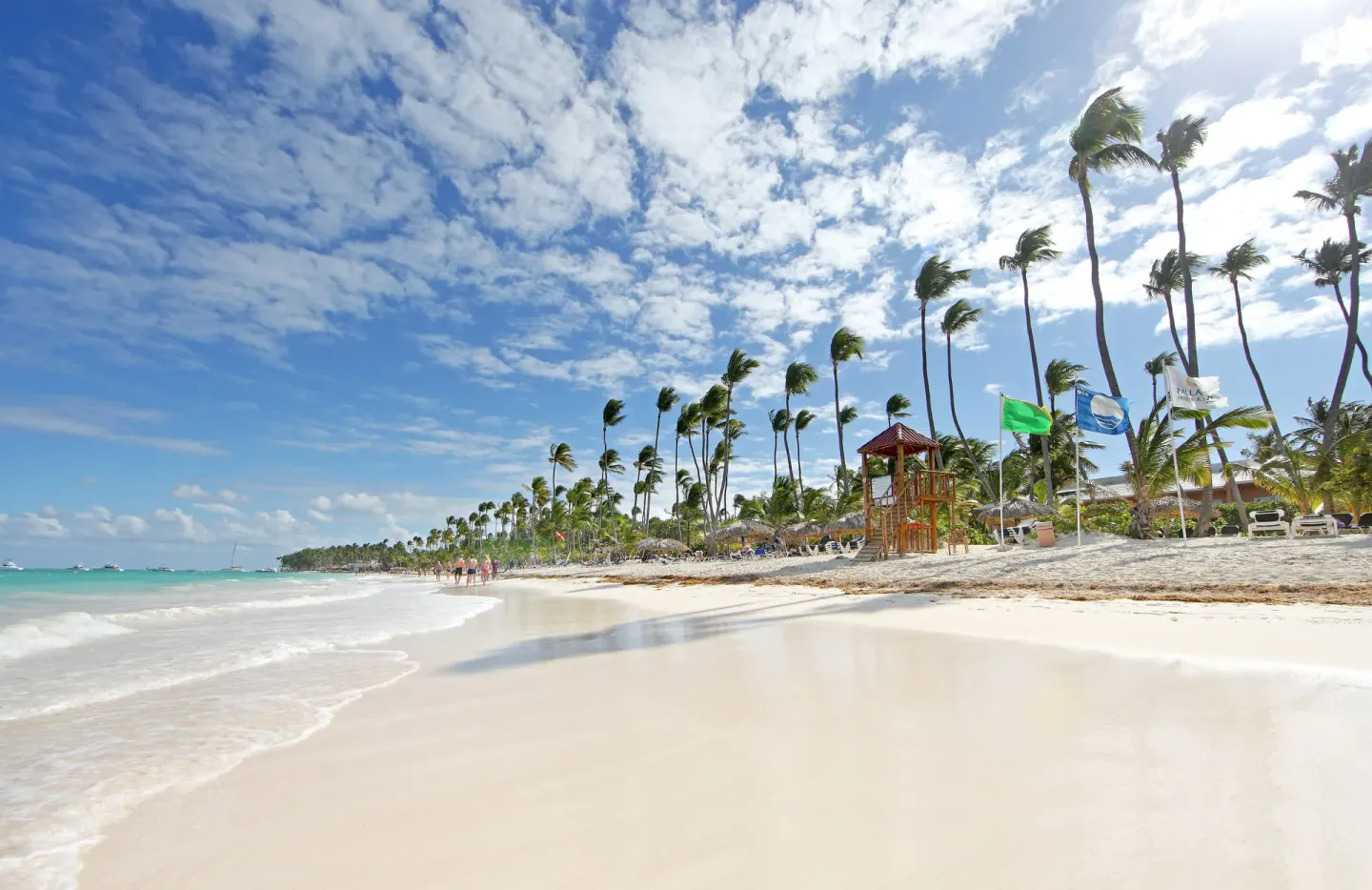 Sandy beach with palms, turquoise water, and a lifeguard tower at Grand Palladium Select Bávaro.