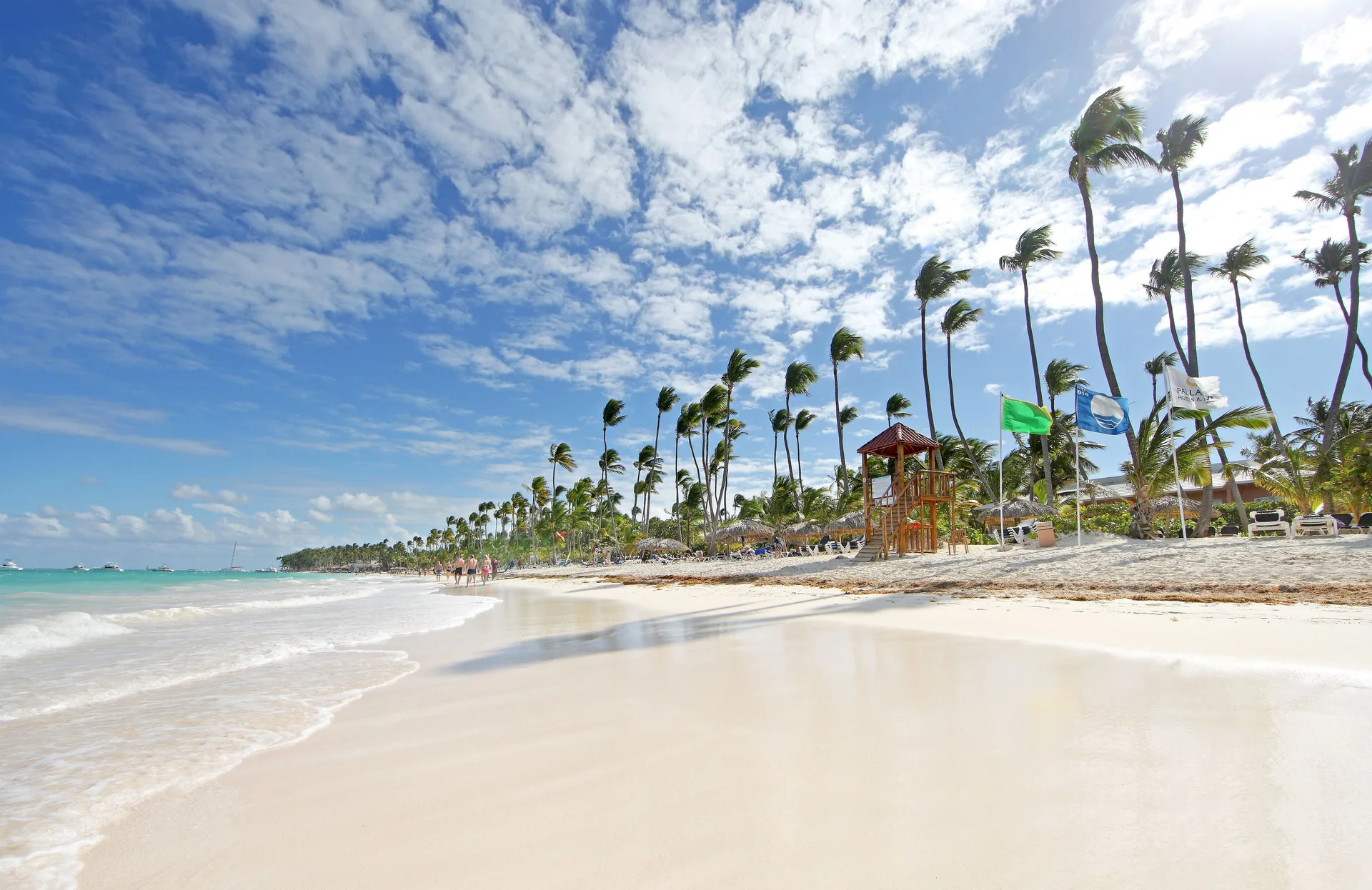 Sandy beach with palms, turquoise water, and a lifeguard tower at Grand Palladium Select Bávaro.