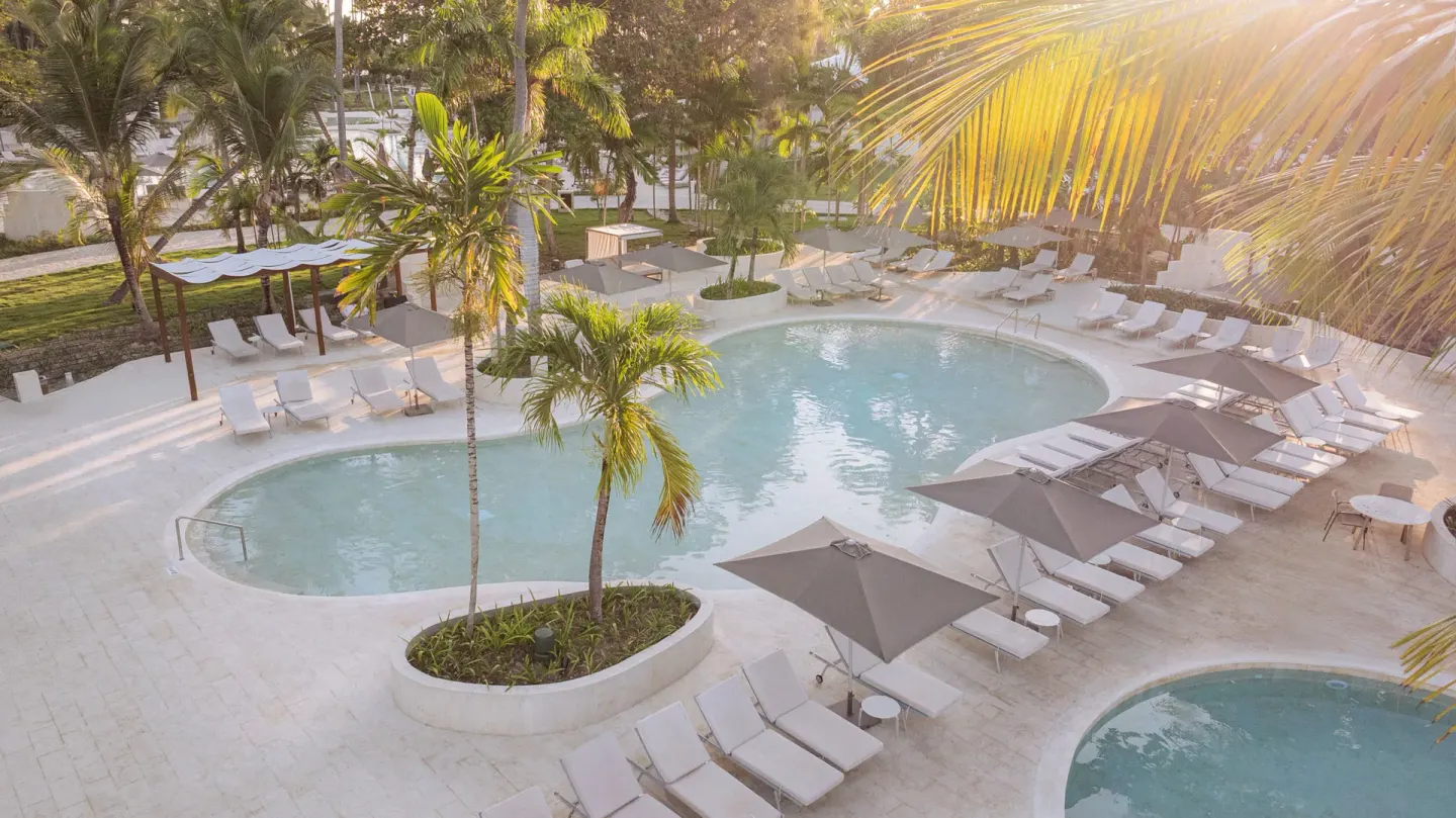 Palm-lined pool deck with loungers and umbrellas at Grand Palladium Select Bávaro.